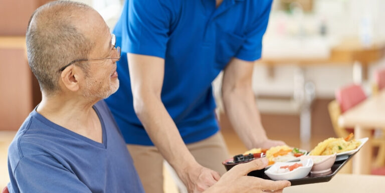 Staff Member Serving Warm Meal Tray at Memory Care Facility